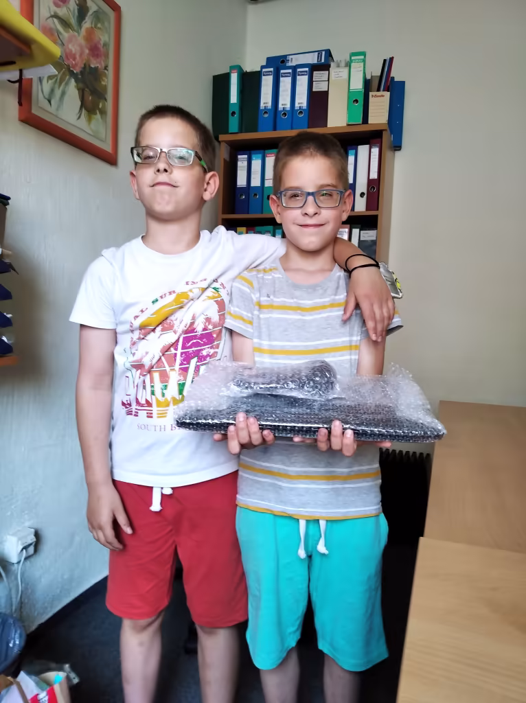 A képen szereplő ikerpár átveszi az adomány laptopot az INFOALAP irodájában
