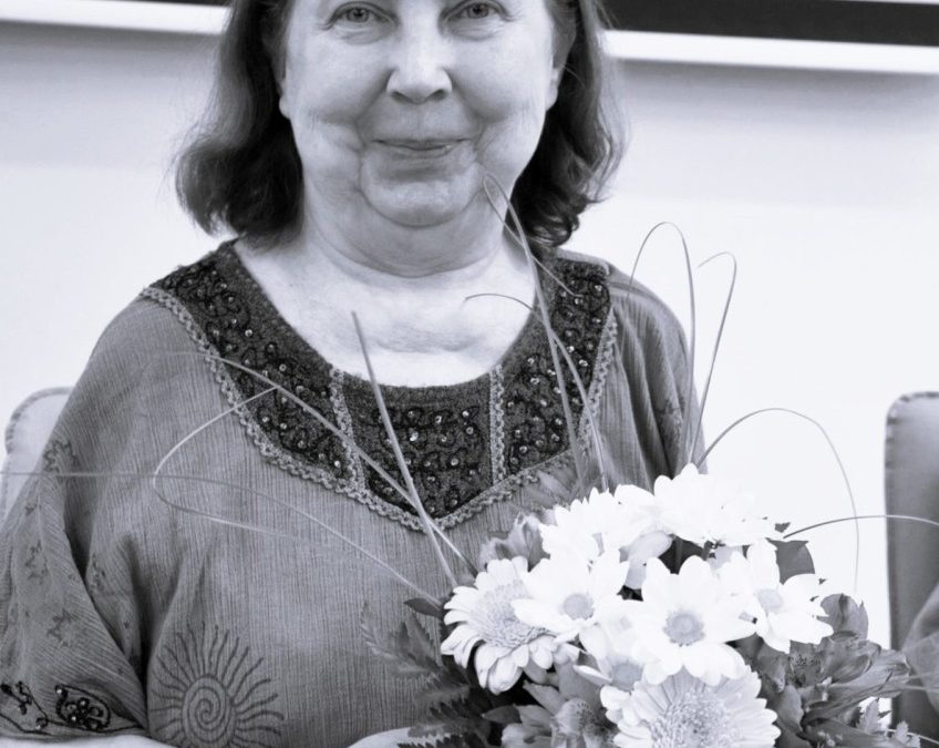 Elhunyt Dr. Gyimesiné Dobos Marianna - a kép fekete-fehér. Mariann mosolyogva egy virágcsokrot tart a kezében. forrás VGYKE